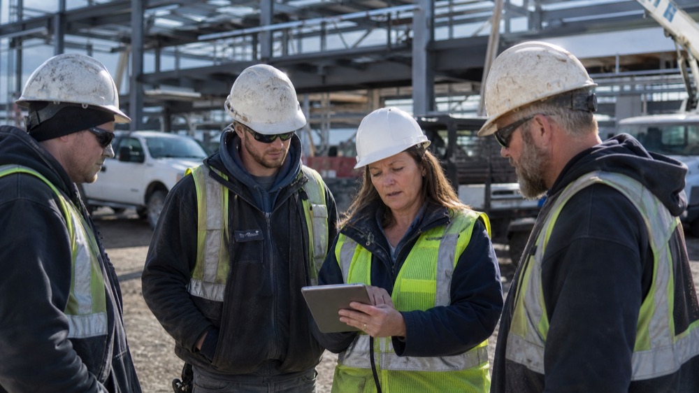 A safety manager reviews a tablet with her crew on a job site